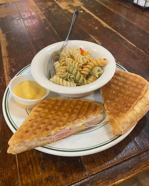 A grilled ham panini with pasta salad on a green-rimmed plate