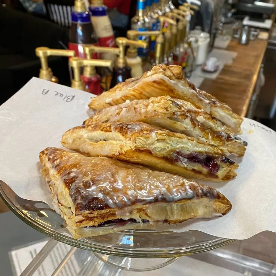 A stack of glazed blueberry turnovers on a glass cake stand